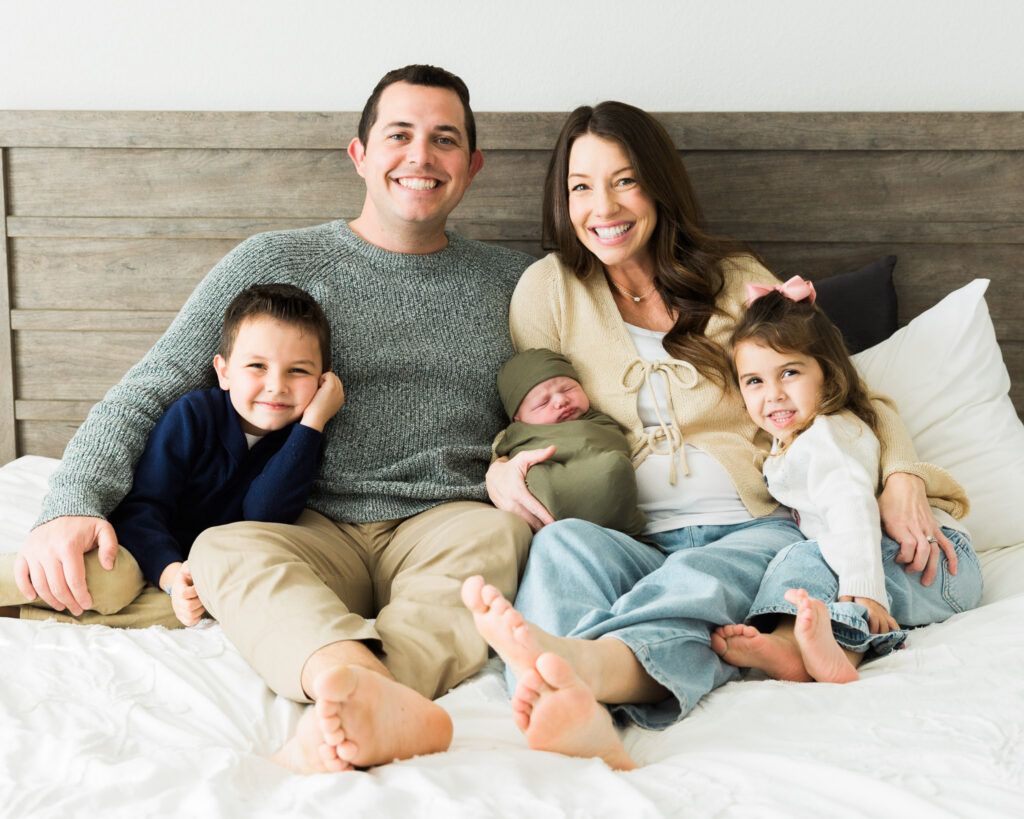 Lowery family sitting together on the bed with their newborn son during family photos at home.