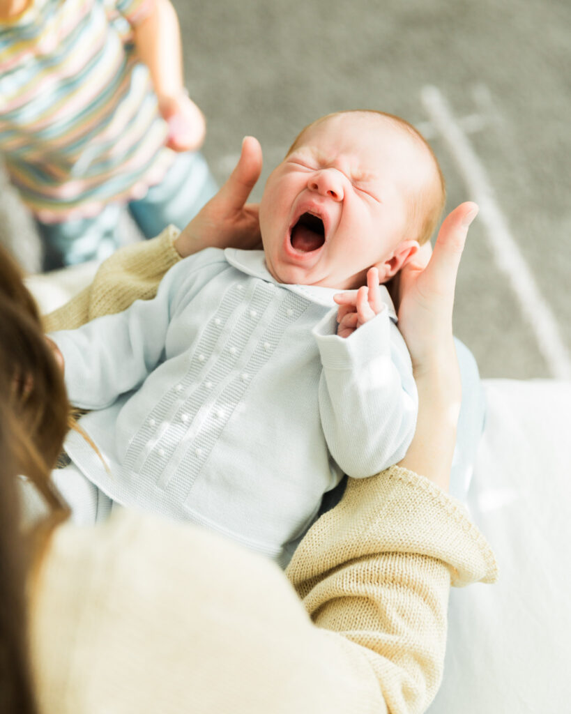 Newborn baby yawning while being held by mom during a lifestyle newborn session.